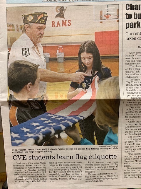 picture of a front-page news article in which a veteran is teaching a group of elementary students how to fold a flag